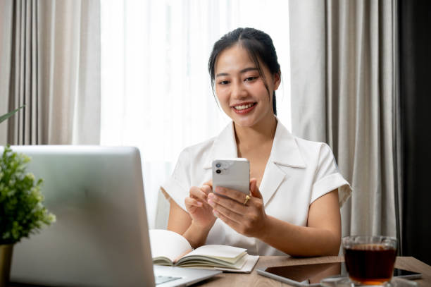 istock Attractive Asian woman using her smartphone at her desk, replying chat, reading blogs on internet. 2162187852