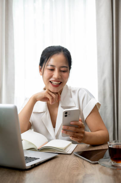 istock Attractive Asian woman using her smartphone at her desk, replying chat, reading blogs on internet. 2162187877