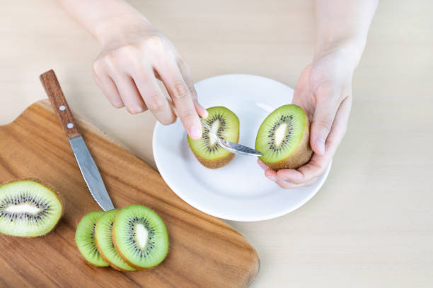 istock A woman is using a spoon to eat a cut green kiwi on the table 2162192187