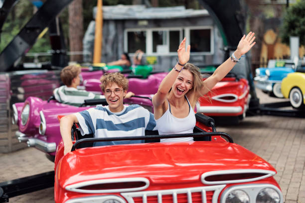 Teenage boy and teenage girl having fun in a car ride carousel in an amusement park. The teenagers are laughing and cheering on a sunny summer day, while spinning on the carousel.\nShot with Canon R5