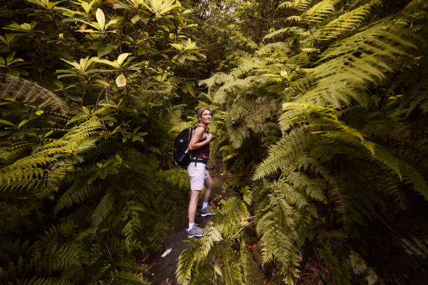 Smiling female backpacker day dreaming while standing among greenery in the forest.