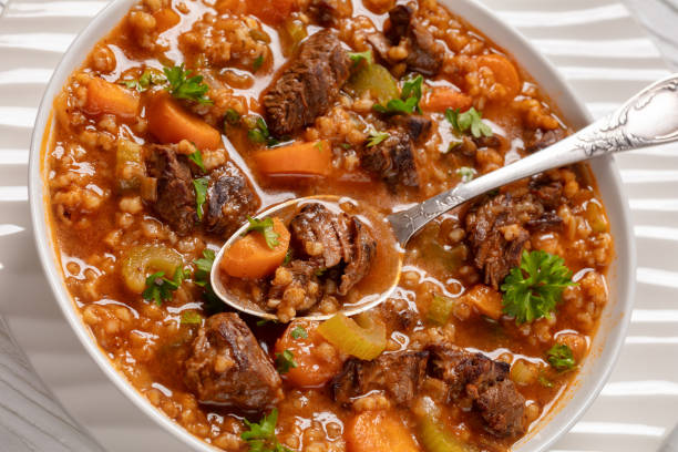 beef barley soup with tender chunks of roast beef, fresh veggies and seasoned broth in white bowl, close-up