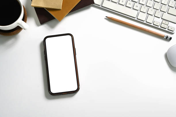 istock Top view a smartphone with blank screen, coffee cup and office supplies on white table 2162203442