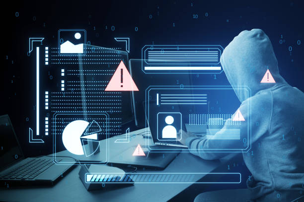 istock A hooded figure using a laptop with cyber security graphics overlay, symbolizing a cyber attack on a dark blue background 2162210508