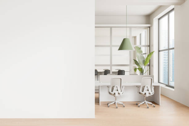 istock Modern office interior with white desks, chairs, green pendant lamp, and large windows, empty white wall on left, minimalistic design concept.  3D Rendering 2162214083