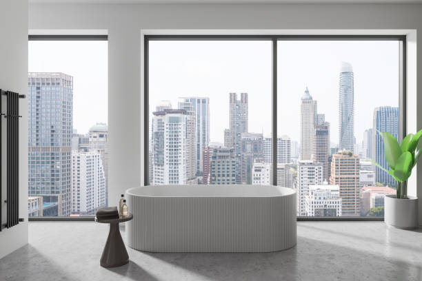 istock Modern hotel bathroom interior with tub, table with accessories and window 2162214567