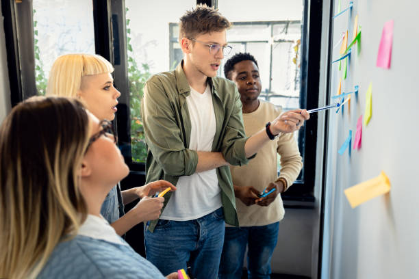 istock Diverse group of young business people working in office using colorful sticky notes on wall to organize their ideas. 2162217645