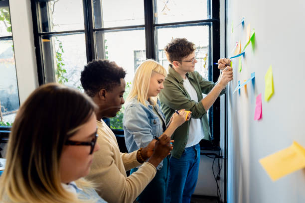 istock Diverse group of young business people working in office using colorful sticky notes on wall to organize their ideas. 2162217651