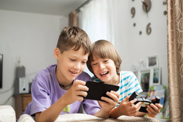 Two Caucasian boys in the living room are looking at a smartphone and smiling, laughing Two Caucasian boys in the living room are looking at a smartphone and smiling, laughing. spy games stock pictures, royalty-free photos & images