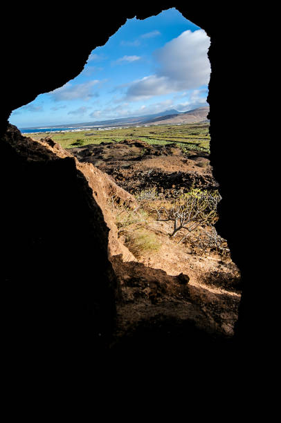 A large rock with a small hole in it. The hole is in the middle of a rocky hillside. The sky is blue and the sun is shining