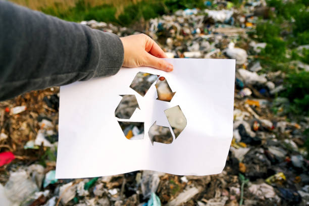 Hand holding a recycle logo against a garbage dump background. Suitable for environmental awareness campaigns