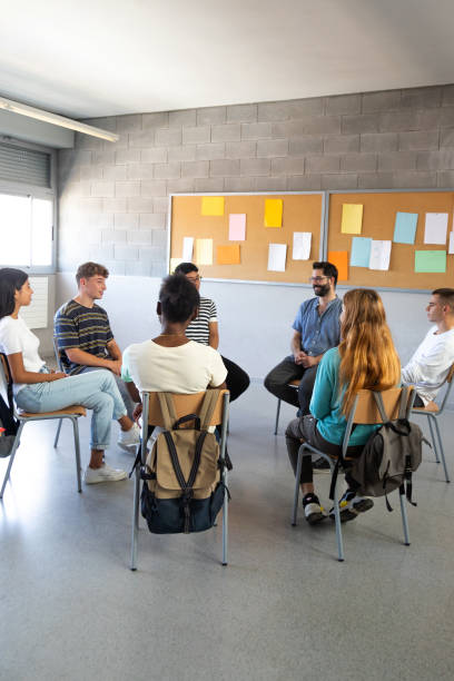 istock High school students sitting in a circle sharing problems with classmates and teacher. Support group. Vertical image. 2162226700