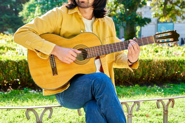 istock unrecognizable Hispanic man playing guitar on bench in a sunny park 2162233421