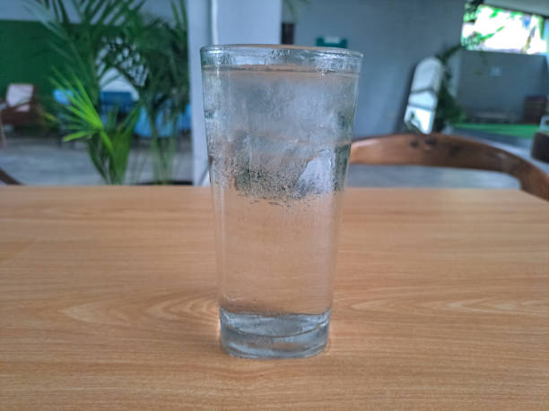 Glasses of water and a bottle on a table at a restaurant next to a window.