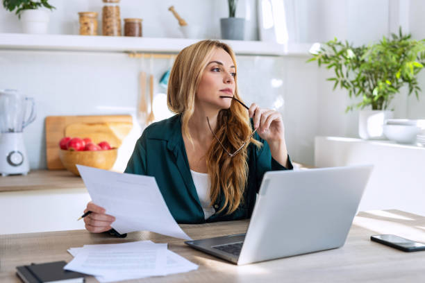 istock Beauty young business woman working with computer while looking forwards in the kitchen at home. 2162233625