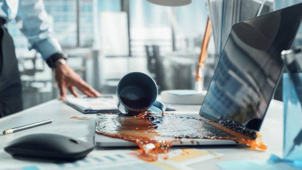 Clumsy Office Worker Accidentally Spilling Hot Coffee on Working Laptop Computer with Business Presentation Or Financial Reports For Large Company. Concept of Failing or Screwing Up In A Workplace