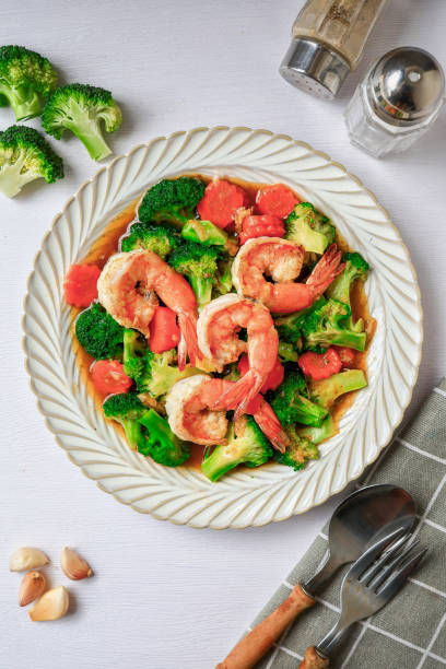 Stir fried broccoli with shrimp in a white ceramic plate witn spoon and fork on white table background
