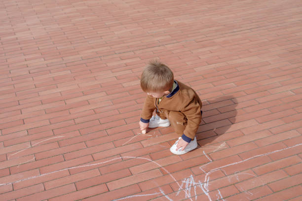 Little boy doodling with chalk on pavement, overhead view