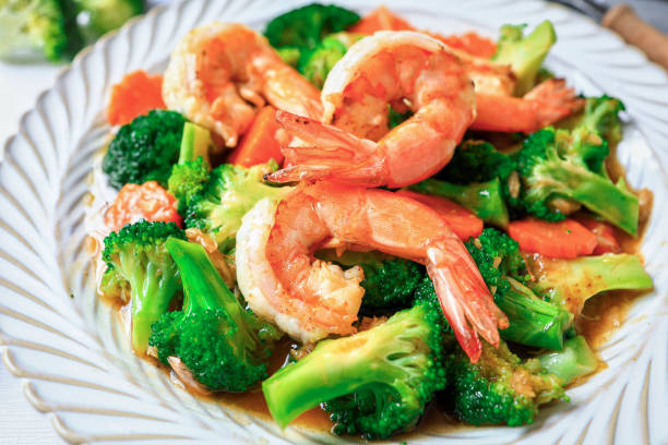 Stir fried broccoli with shrimp in a white ceramic plate witn spoon and fork on white table background