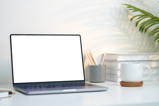 istock Laptop with blank screen, books and cup of coffee on white table with warm light. 2162240570