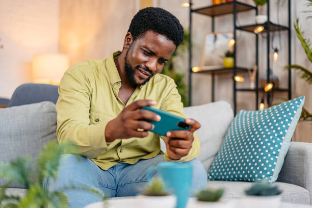 istock Young Man Playing Video Games On The Phone While Sitting On The Sofa At Home 2162244341