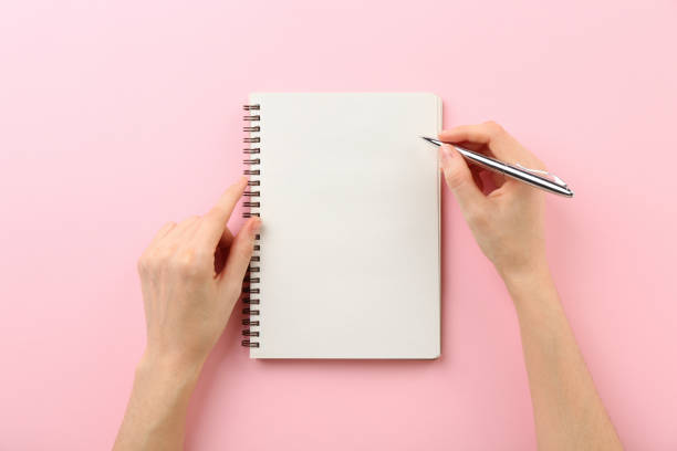istock Woman writing in notebook on pink background, top view 2162245916