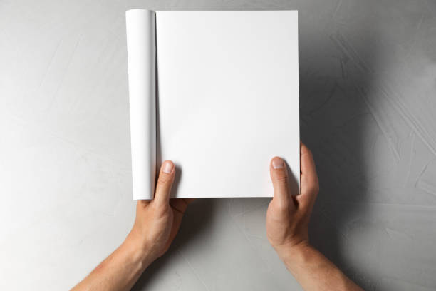 istock Man holding blank notebook at light grey table, top view. Mockup for design 2162246585