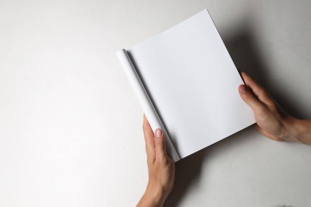 istock Man holding blank notebook at white table, top view. Mockup for design 2162246603