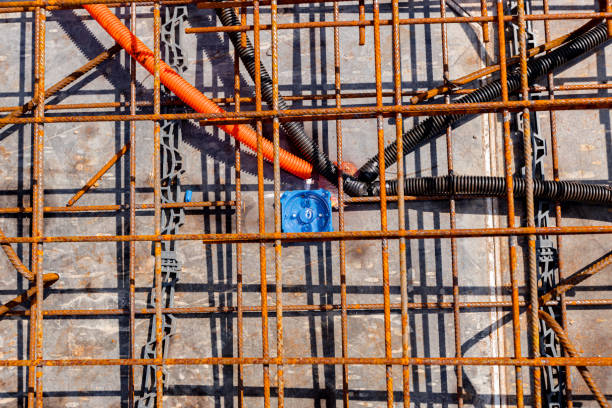 Messy coil of gray electrical conduit pipes lying on bare ground and rubble by an unfinished brick building, ideal for construction, industrial, utility, infrastructure background, maintenance, or renovation themes.
