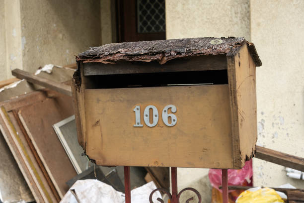 Old damaged brown wooden mailbox with rubbish behind.