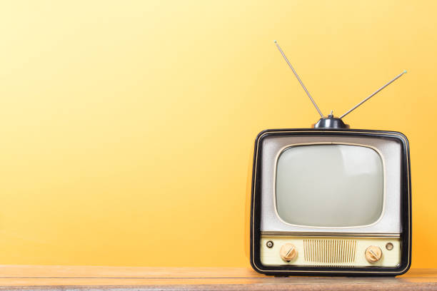 Retro television on old wooden table front gradient yellow background. Vintage style filtered photo