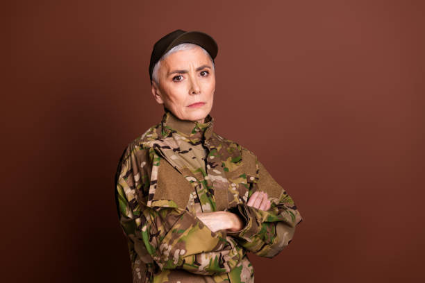 istock Photo of serious confident elderly lady dressed camo uniform arms folded empty space isolated brown color background 2162256647