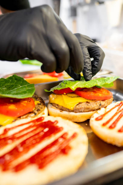 istock Close-up of hands assembling a freshly prepared cheeseburger with lettuce, tomato, and sesame bun, showcasing fast food preparation 2162261776