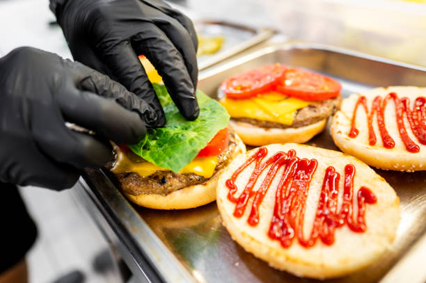 istock Close-up of hands assembling a freshly prepared cheeseburger with lettuce, tomato, and sesame bun, showcasing fast food preparation 2162261786