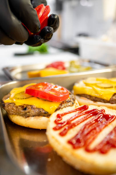 istock Close-up of hands assembling a freshly prepared cheeseburger with lettuce, tomato, and sesame bun, showcasing fast food preparation 2162261792