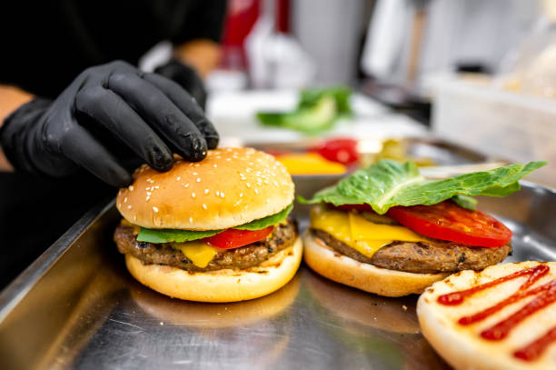 istock Close-up of hands assembling a freshly prepared cheeseburger with lettuce, tomato, and sesame bun, showcasing fast food preparation 2162261803