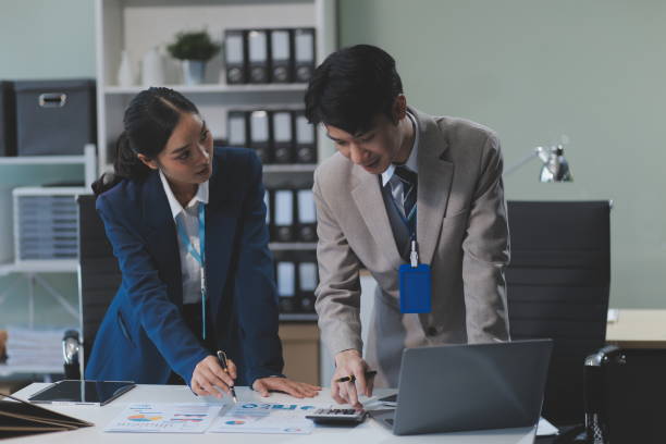 istock Cheerful businesspeople using a laptop in an office. Happy young entrepreneurs smiling while working together in a modern workspace. Two young businesspeople sitting together at a table. 2162274132