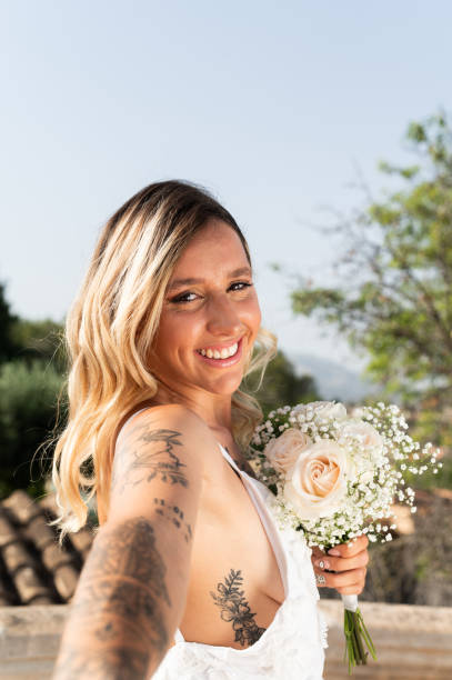 Vertical side view and personal perspective of a bride taking a selfie smiling holding a bouquet outdoors