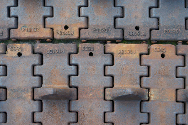 This detailed image captures a close-up view of rusty tank tracks, showcasing the intricate patterns and textures formed by corrosion over time. The weathered metal pieces tell a story of past military machinery, now aged and marked by the elements. The interconnected design of the tracks highlights their robust engineering, even as nature slowly reclaims them.