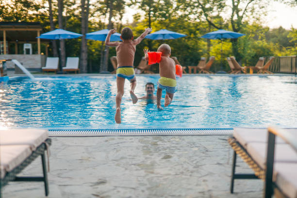 istock Two boys are jumping into the pool while their dad waits in the pool. 2162282351
