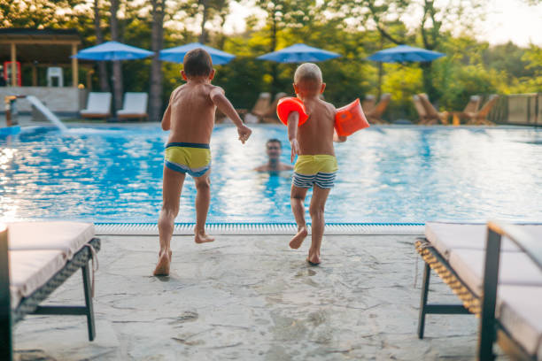 istock Two boys are jumping into the pool while their dad waits in the pool. 2162282453
