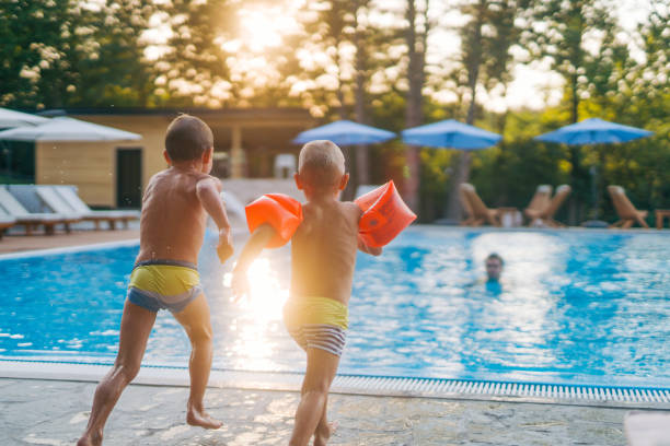 Two boys are jumping into the pool while their dad waits in the pool.