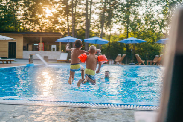 istock Two boys are jumping into the pool while their dad waits in the pool. 2162282648