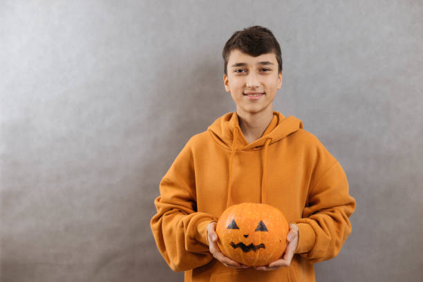 Protret a young man with a pumpkin to Halloween in his hands on a gray background. Copy space