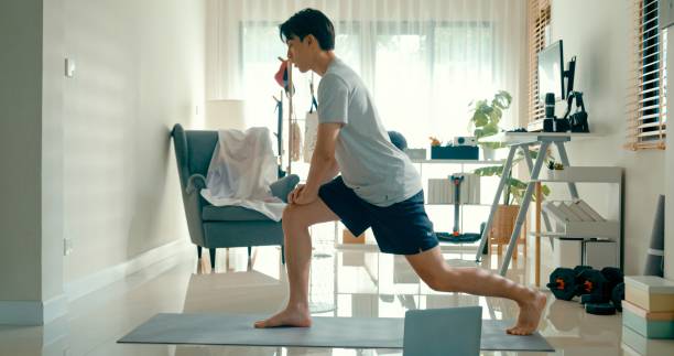 istock Young Asian athletic man lunging stretch during a home workout, utilizing a laptop for online fitness instruction. Diet and exercise morning routine. 2162293394