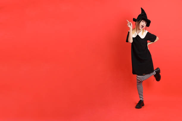 Portrait of a young woman dressed like an evil witch using magic cane and practicing magic in the forest at night.