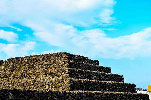 A stone pyramid with a blue sky in the background. The pyramid is made of stone and has a very old look to it