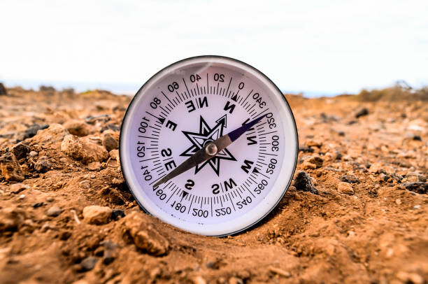 A compass is laying on the ground in a desert. The compass is pointing to the north. The desert is barren and rocky, with no vegetation in sight. The compass is the only object in the scene