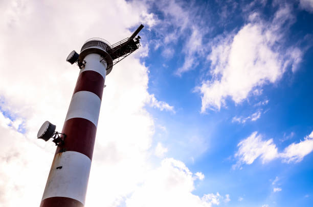 A tall red and white lighthouse is standing in the sky. The sky is blue with some clouds