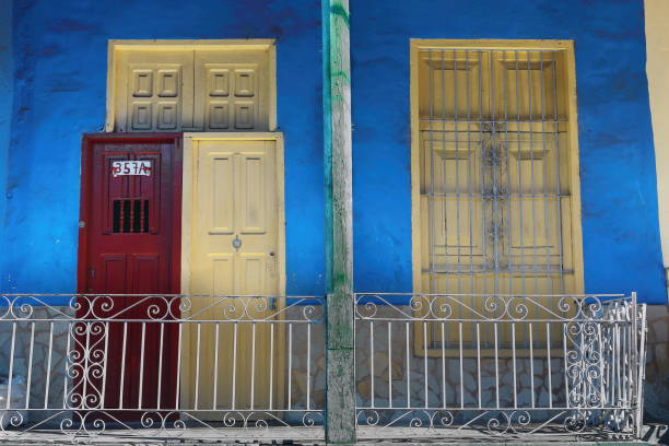 Santiago, Cuba-October 20, 2019: South-facing facade porch of one-storey Colonial style house on Calle Heredia Street featuring azure-blue wall, grille-covered window and red-yellow wooden doors.